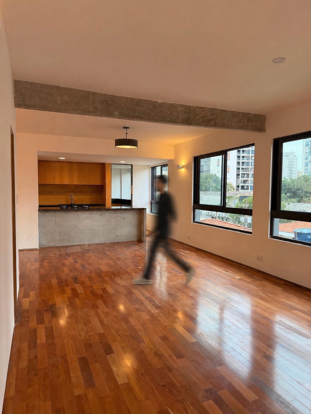 Interior do apartamento — piso de madeira, janelões e cozinha integrada